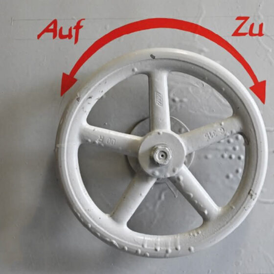 Ein Handrad an einer grauen Maschine mit der Beschriftung „Auf“ und „Zu“ und einem Pfeil in zwei Richtungen weisend