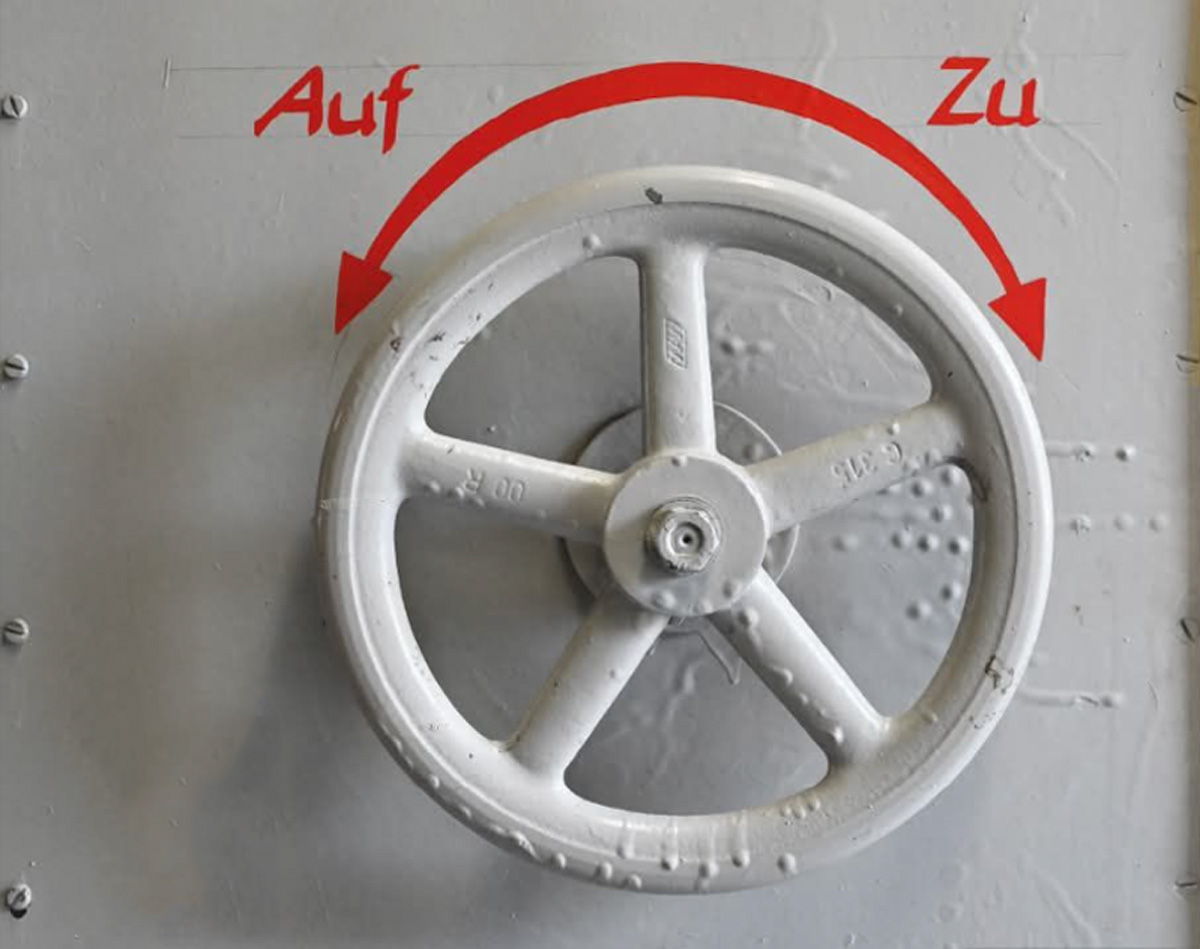 Ein Handrad an einer grauen Maschine mit der Beschriftung „Auf“ und „Zu“ und einem Pfeil in zwei Richtungen weisend